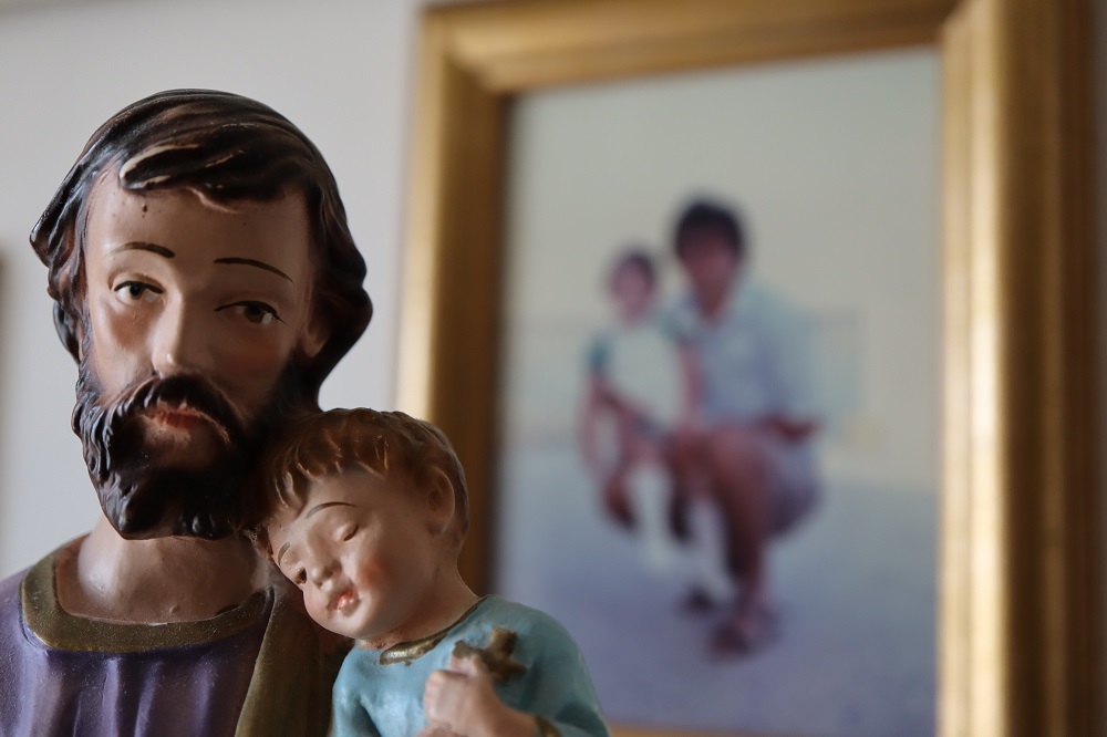 Statuetta di san Giuseppe con Bambino Gesù dormiente e sullo sfondo una foto di un papà con la sua bambina